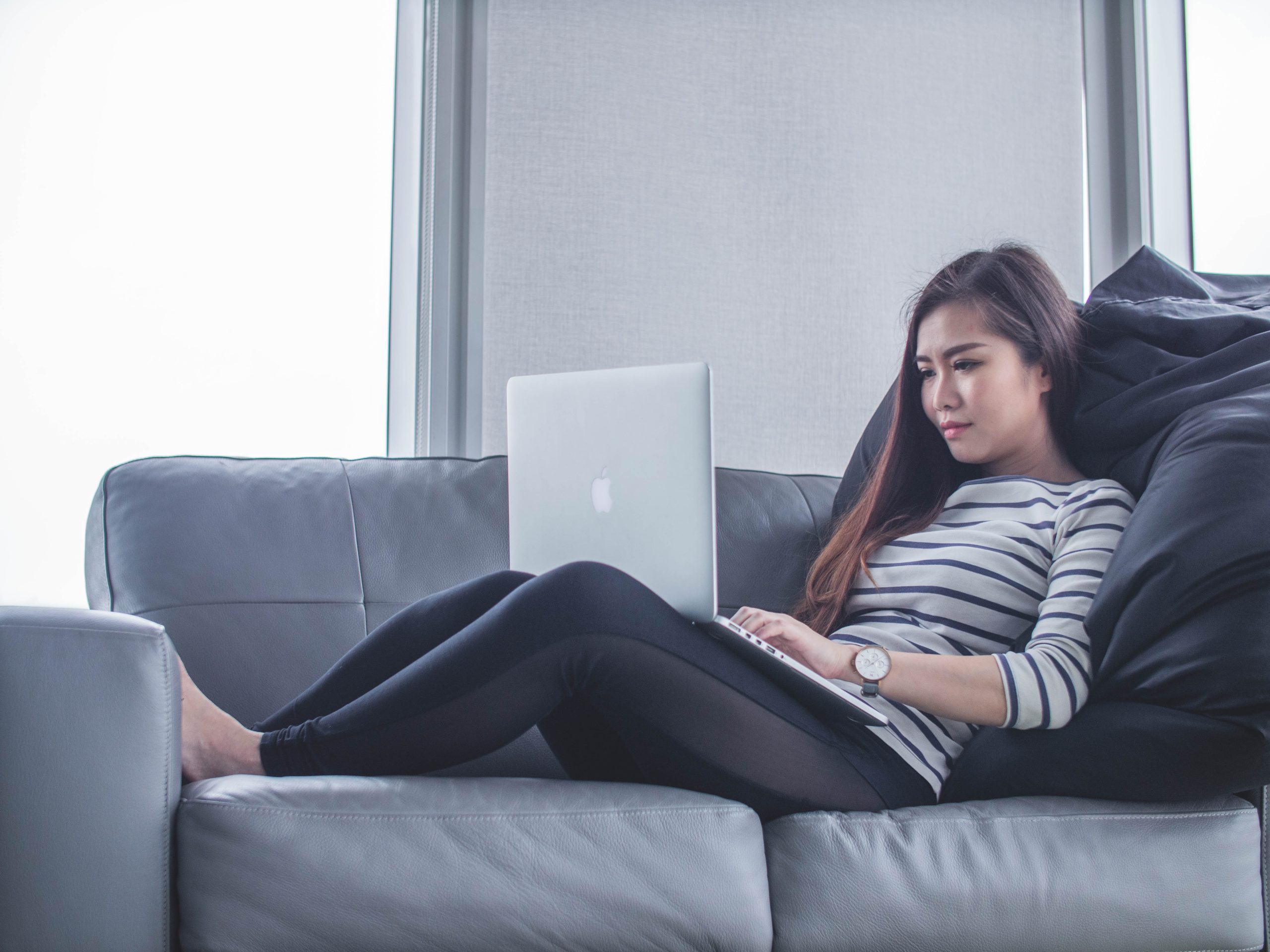 Woman working on laptop and lying on sofa